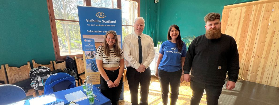 Photo taken at the launch event of Sight Loss Councils Scotland. From left to right: Lara, SLC volunteer, Iain Mitchell, Senior Engagement Manager for Sight Loss Councils North, Emma Scott, Head of Operations, Visibility Scotland, and Callum Lancashire, Engagement Manager for Sight Loss Councils Scotland. They are stood together next to a Visibility Scotland banner, smiling at the camera.