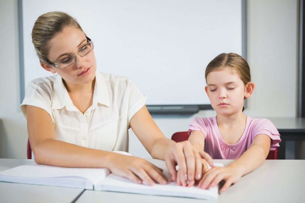 A woman helping a young girl with reading braille