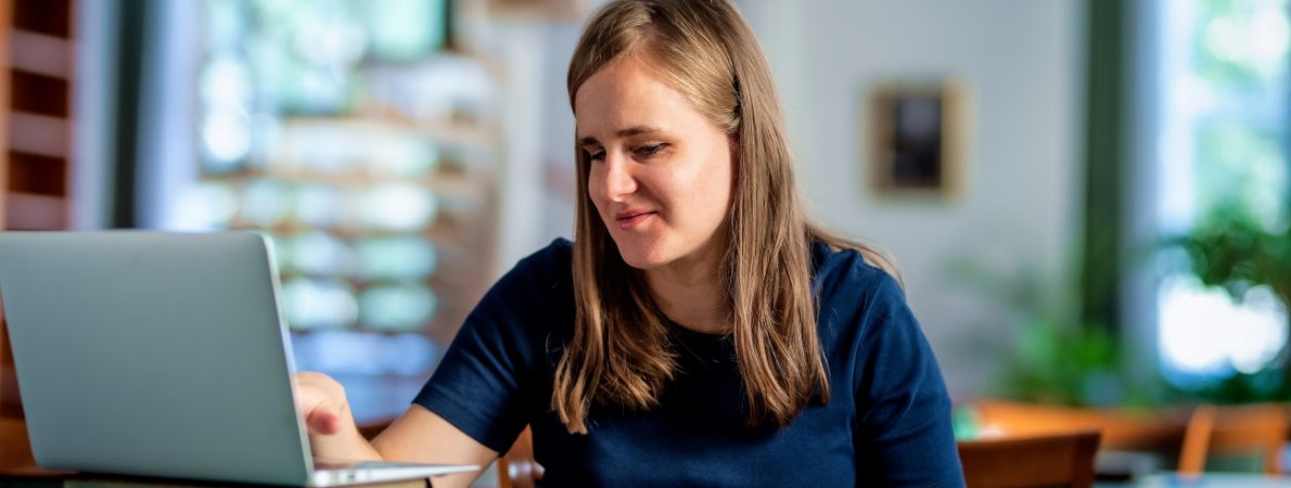 A visually impaired woman sitting and studying in the university library using laptop and books