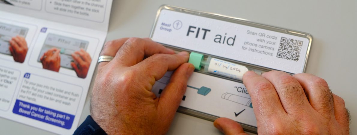A pair of hands closing a FIT (Faecal Immunochemical Test) bottle with braille on the FIT aid tool. The hands slide the stick and tube down the accessible channel.