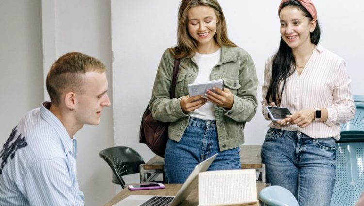 Five students sitting or standing around a table smiling