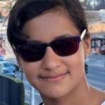 Young Voices volunteer Selvi. Selvi wears tinted glasses and smiles at the camera