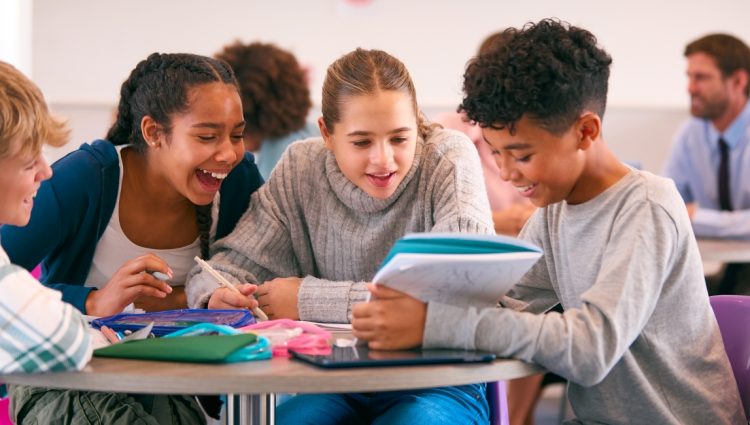 Secondary Or High School Students Collaborating In Study Area With Teachers In Background