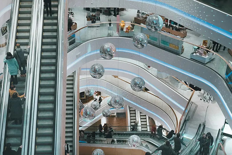 The inside of a shopping centre seen from above withg multiple escalators linking the floors. There are glitter balls hanging down the centre of the stairwell.