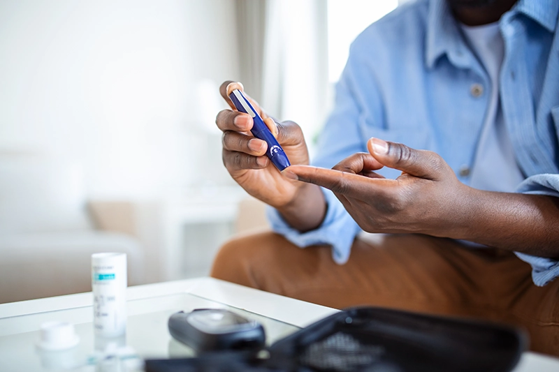 Man is sitting at the sofa at the home and taking blood from his finger for diabetes test