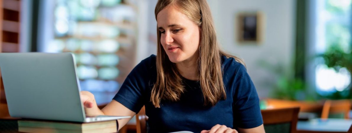 A visually impaired woman sitting and studying in the university library using laptop and books