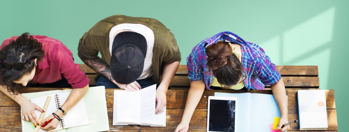 A picture taken from above that shows three young people sitting on a desk and studying