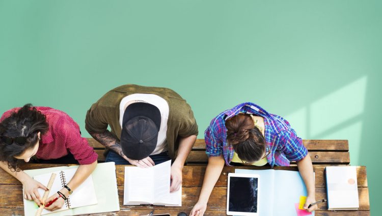 A picture taken from above that shows three young people sitting on a desk and studying