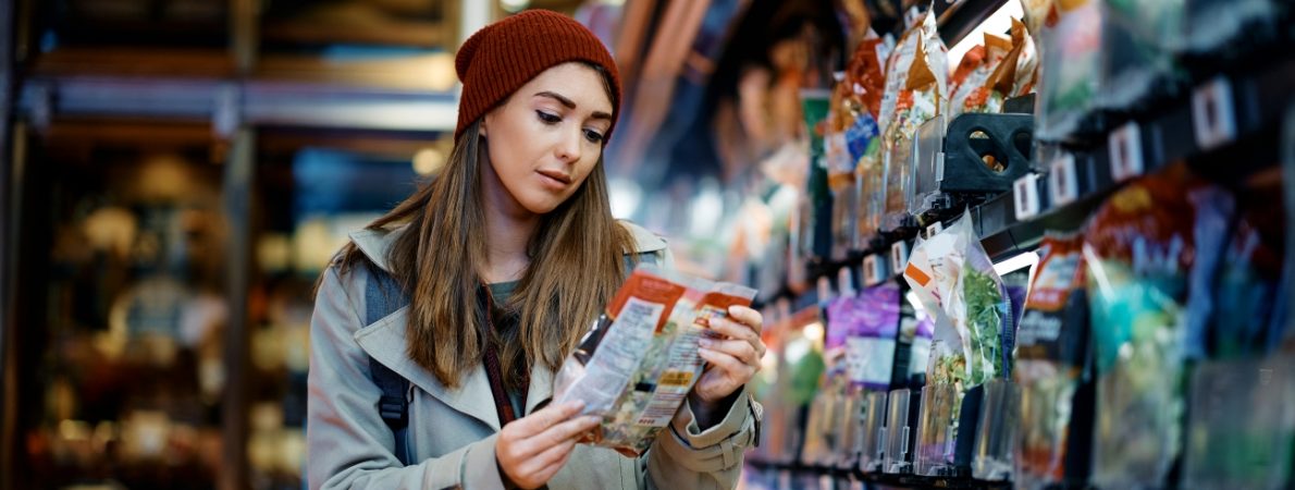 Young woman reading nutrition label on package while shopping food in supermarket.