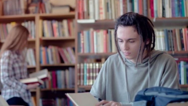 A picture of a student in a library, with books and papers in front of her