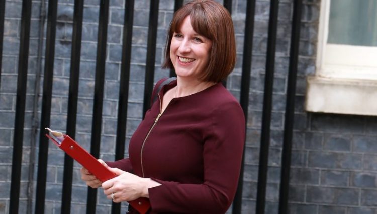 Photo shows Chancellor Rachel Reeves walking and smiling holding her red ministerial folder