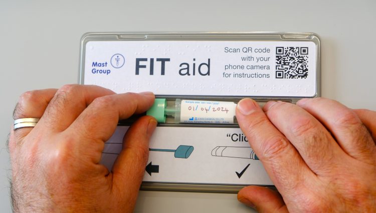 A pair of hands closing a FIT (Faecal Immunochemical Test) bottle with braille on the FIT aid tool. The hands slide the stick and tube down the accessible channel.